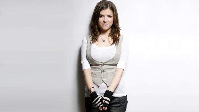 woman wears gray 3 button vest stands behind white painted wall