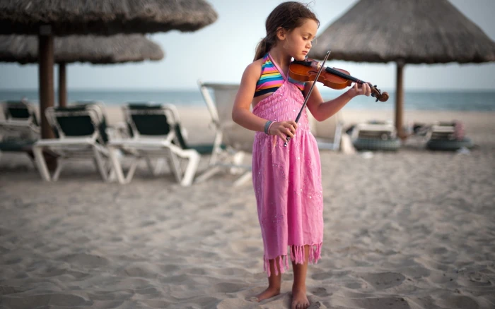Cute little girl at the beach playing a violin 2k