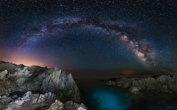 rock cliff with body of water under milky way starry night long exposure