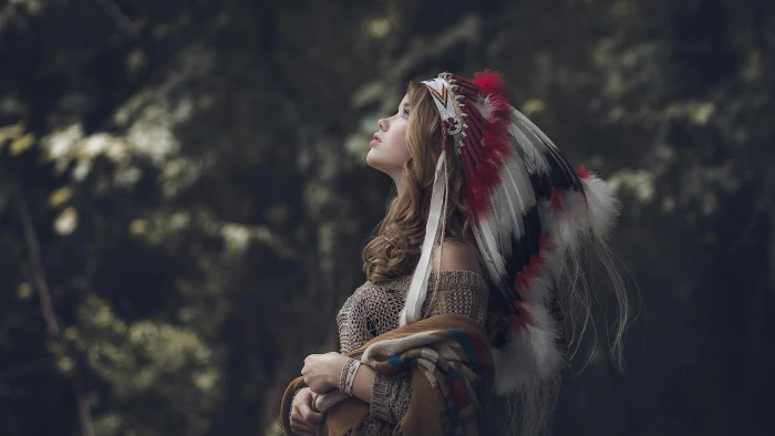 women's gray native American costume woman in white red and black feather headdress looking up 2k