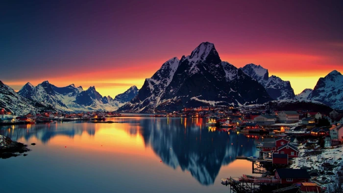town structures and body of water clear calm in front ice covered mountains under orange blue sky 2k