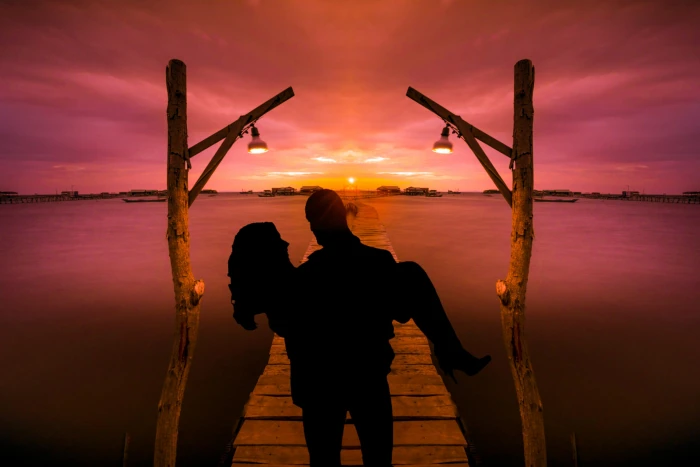 silhouette of man carrying woman on dock near water face to 2k