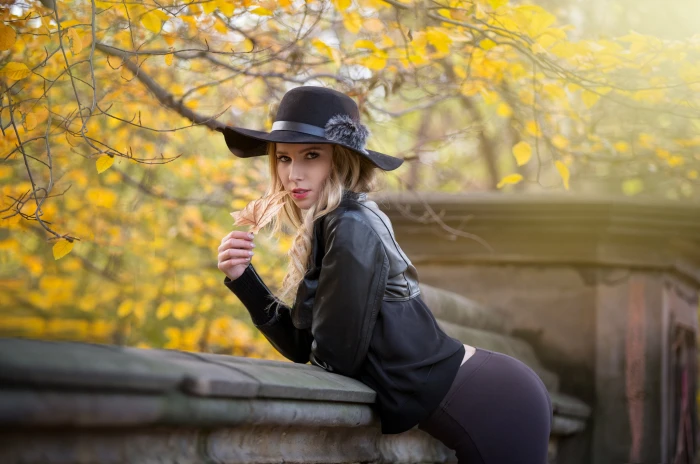 women's black leather jacket woman wearing sun hat standing beside gray concrete rail at daytime 2k