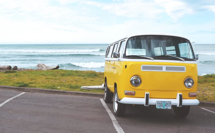 yellow Volkswagen van on concrete road and white bus parked near sea shore under cloudy sky 2k