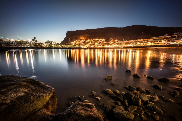 black rocks on body of water near city lights under blue sky during sunset gran canaria canary islands 2k
