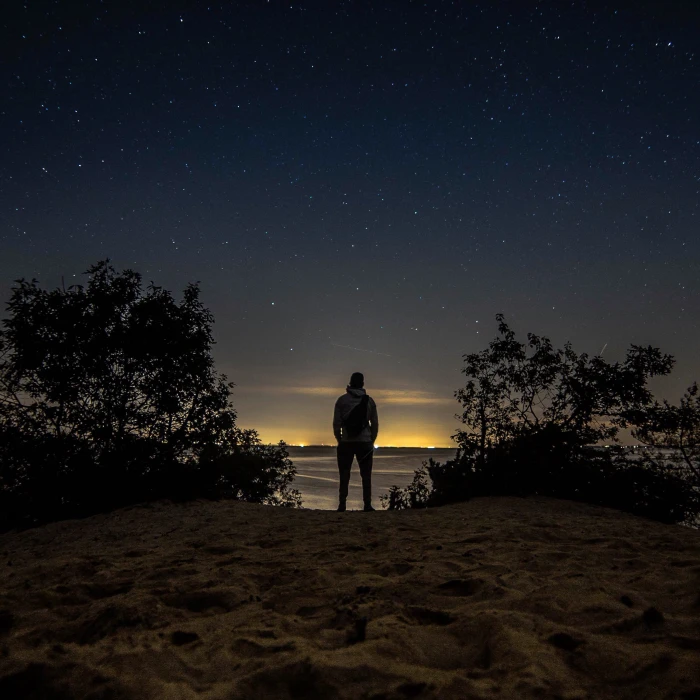 man standing in front of body water staring at the desert under starry night 2k