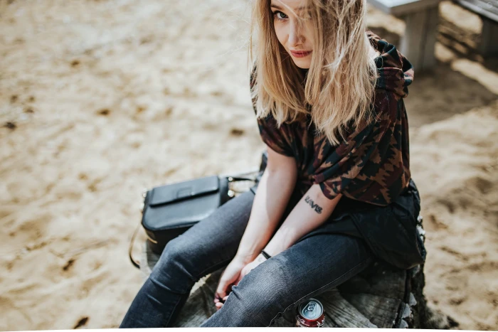 Beautiful blonde woman relaxing with a can of coke on tree stump by the beach 2k 4k