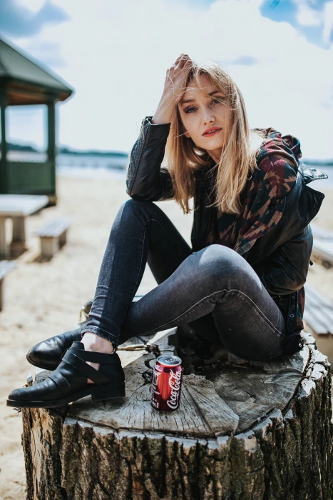 Beautiful blonde woman relaxing with a can of coke on tree stump by the beach 2k