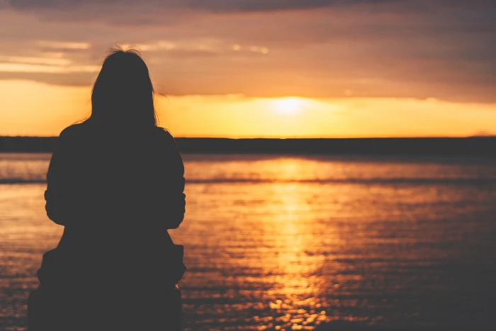 silhouette of woman sitting near bay person facing towards body water during golden time 2k 4k 5k