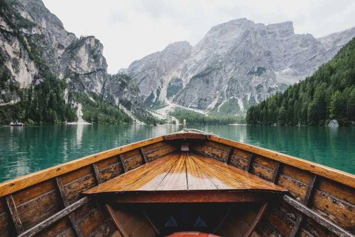 brown wooden boat moving towards the mountain person riding on lake during daytime 2k 4k 5k