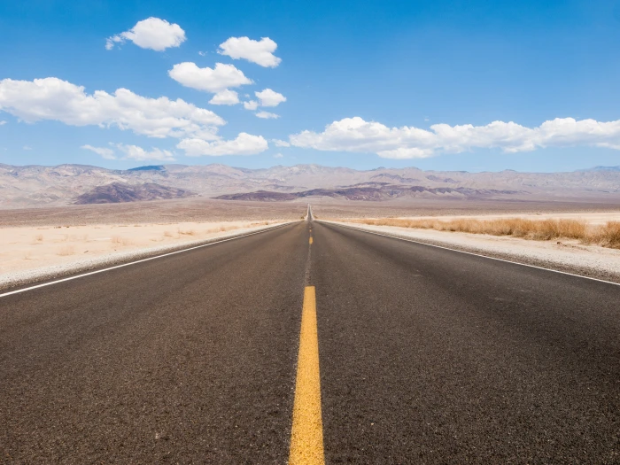 empty black asphalt road between brown field near mountains under blue and white cloudy sky at daytime 2k 4k