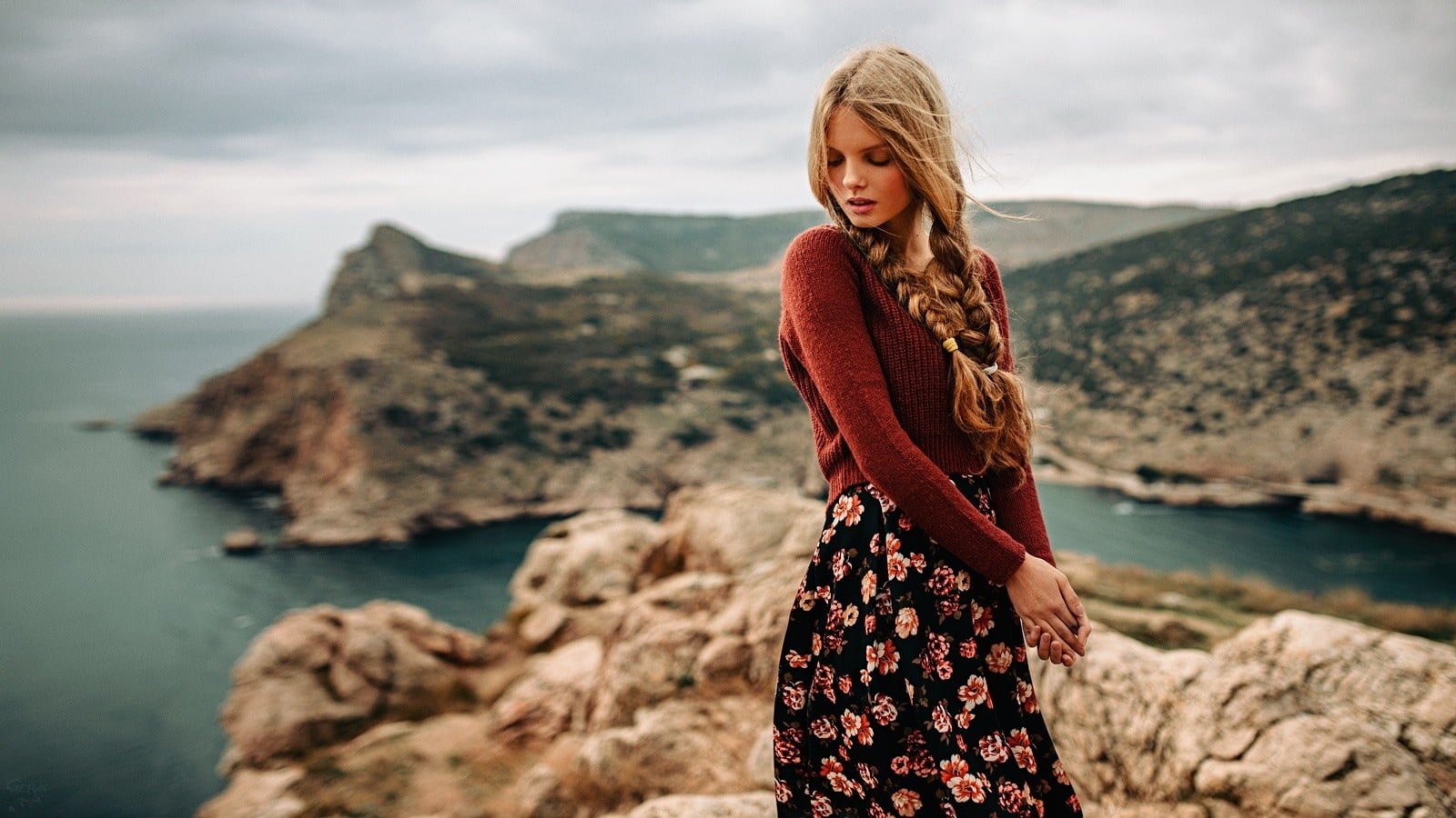 blonde haired woman in brown long sleeve top standing on of mountain beside body water 2k