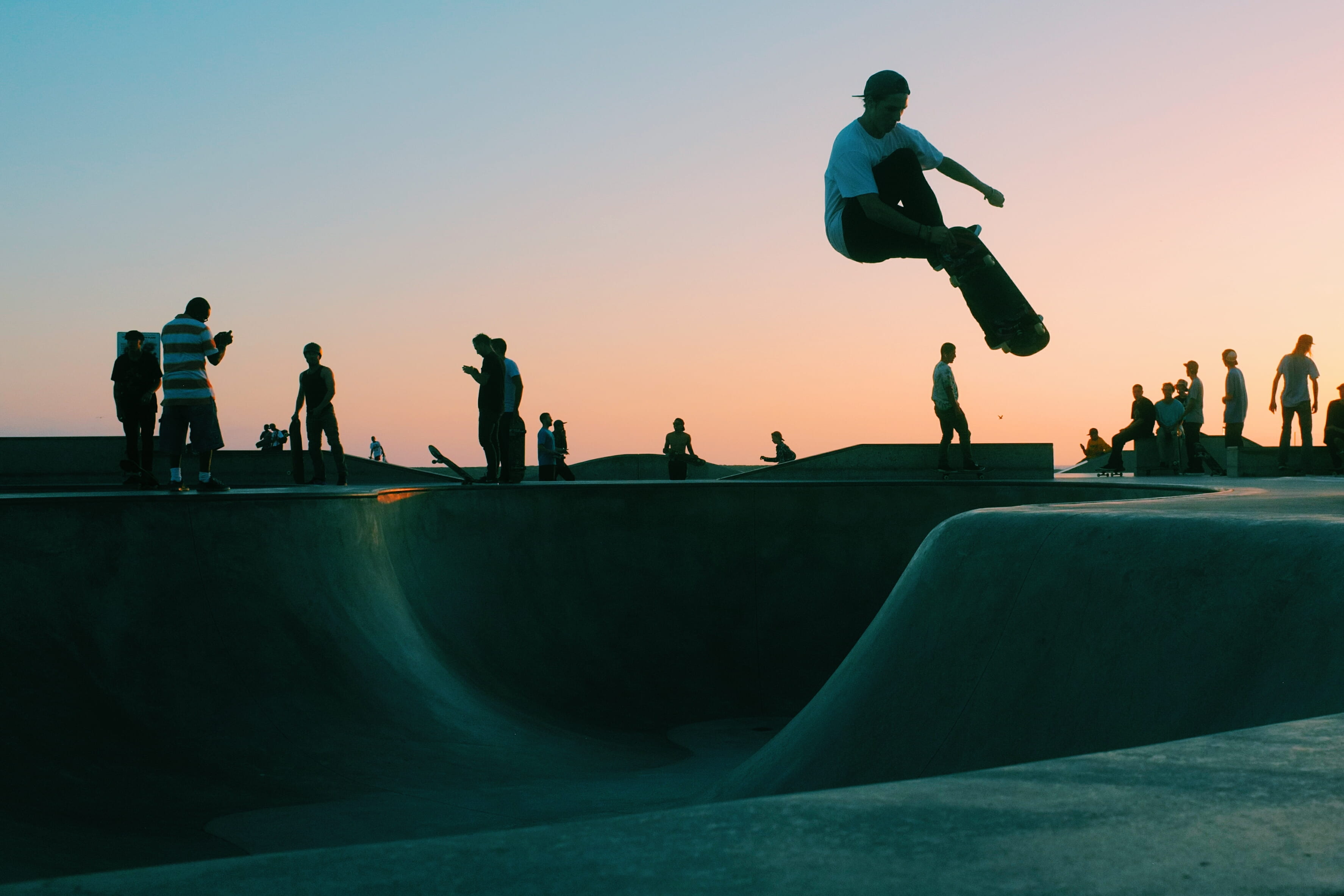 man doing trick at skateboard park during sunset several people playing on skate 2k 4k