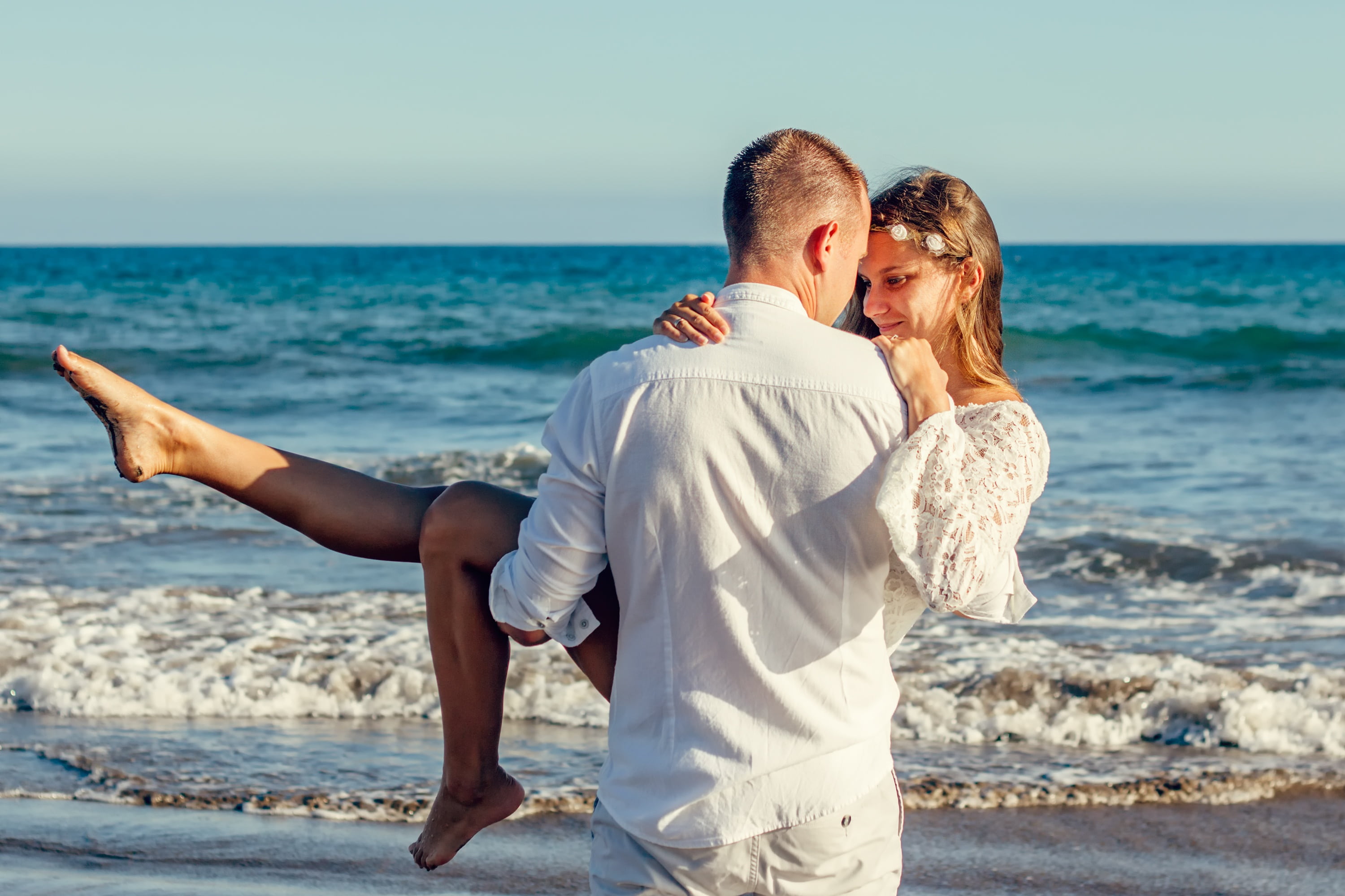 man in white dress shirt carrying a woman top front of sea 2k