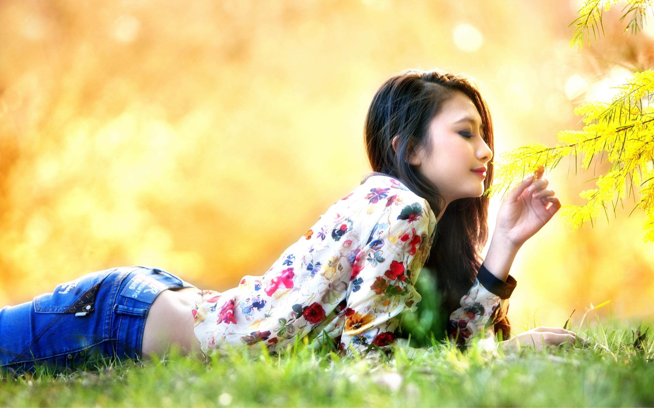 women's white and multicolored floral long sleeved blouse woman lying down on green grass field smelling leaves 2k