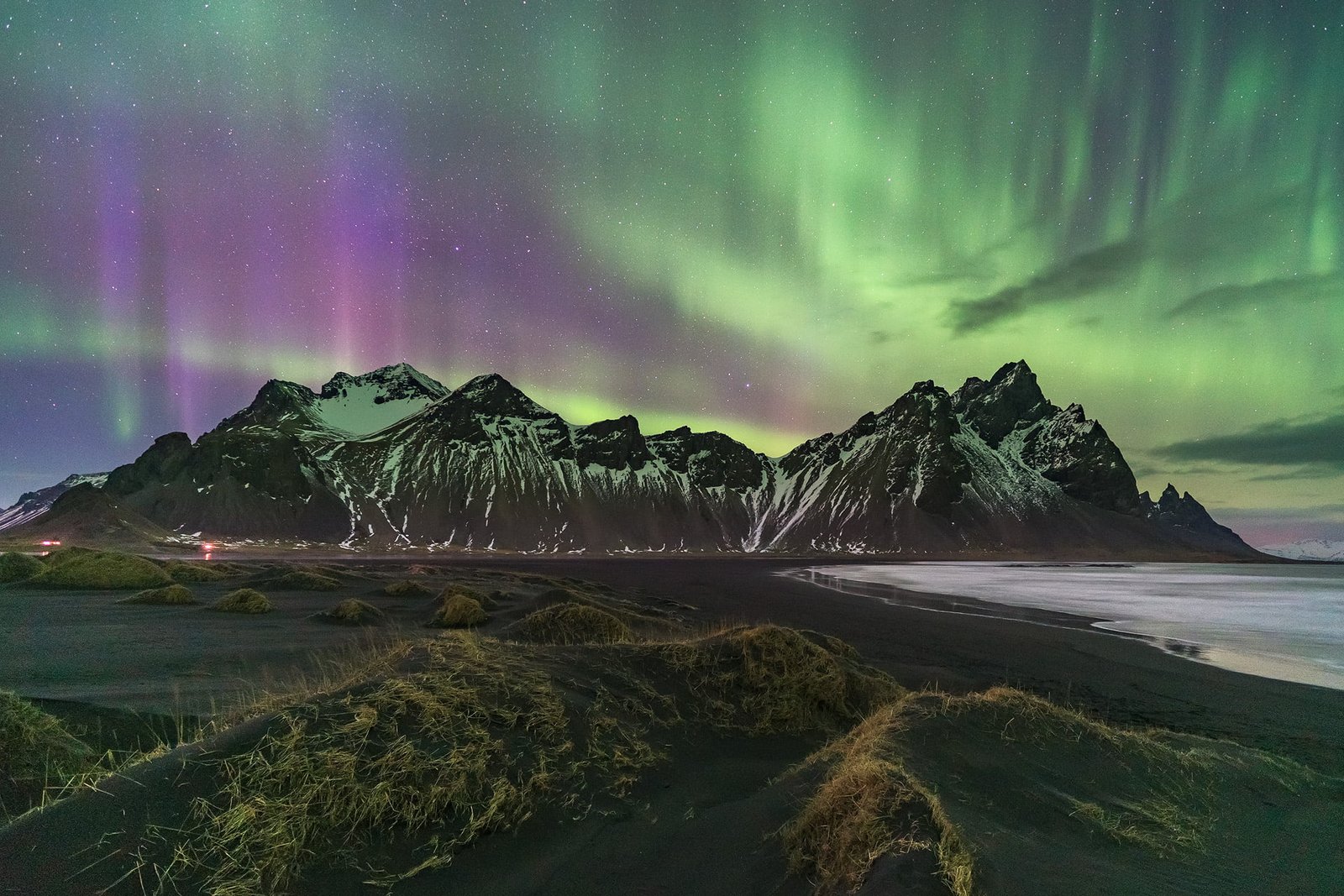 photograph of black mountain under green and purple aurora borealis 2k
