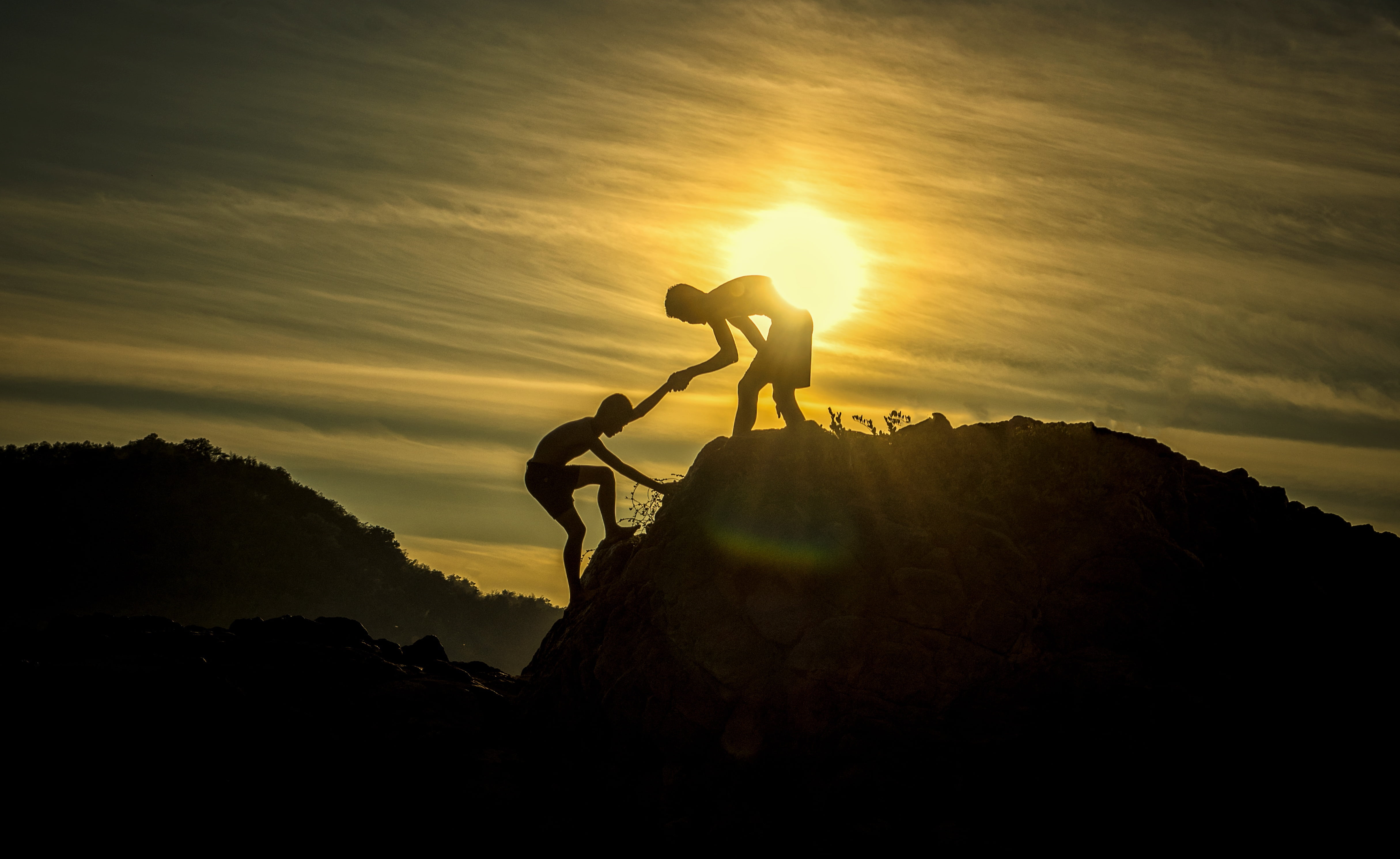 silhouette of man helping another to climb on cliff during golden hour 2k 4k 5k