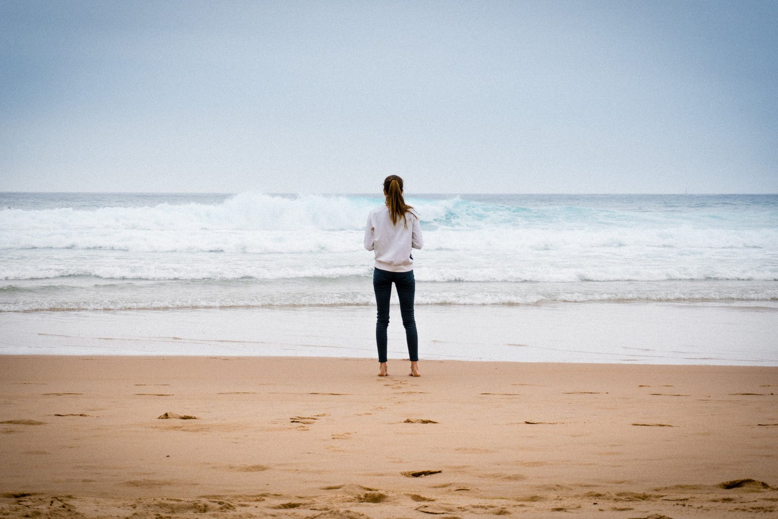 woman standing near seashore during daytime on sand beach 2k