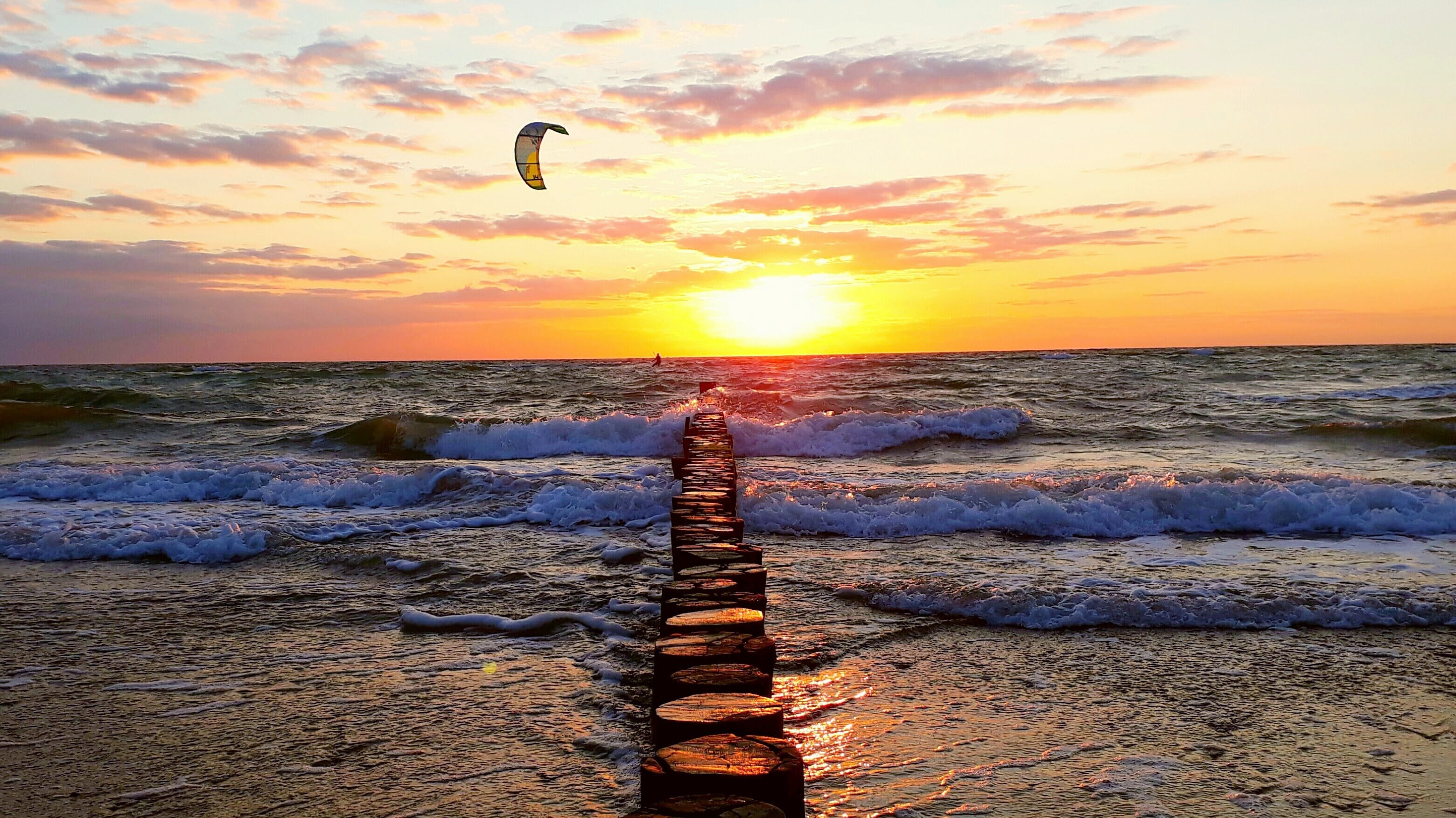 body of water during sunset groynes kitesurfer sea wave evening sun 2k