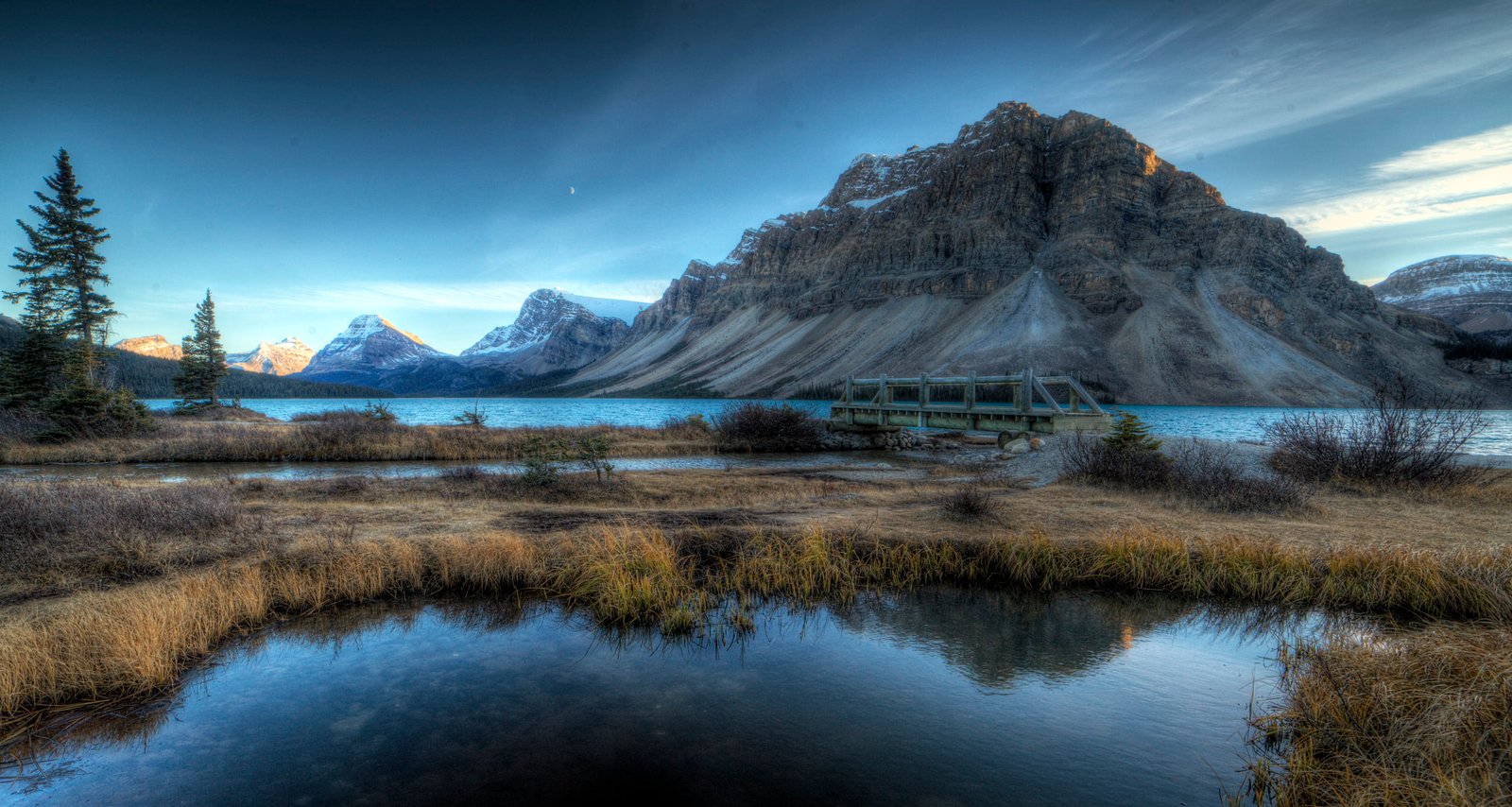 lake between grass field near sea and mountains under gray sky bow 2k