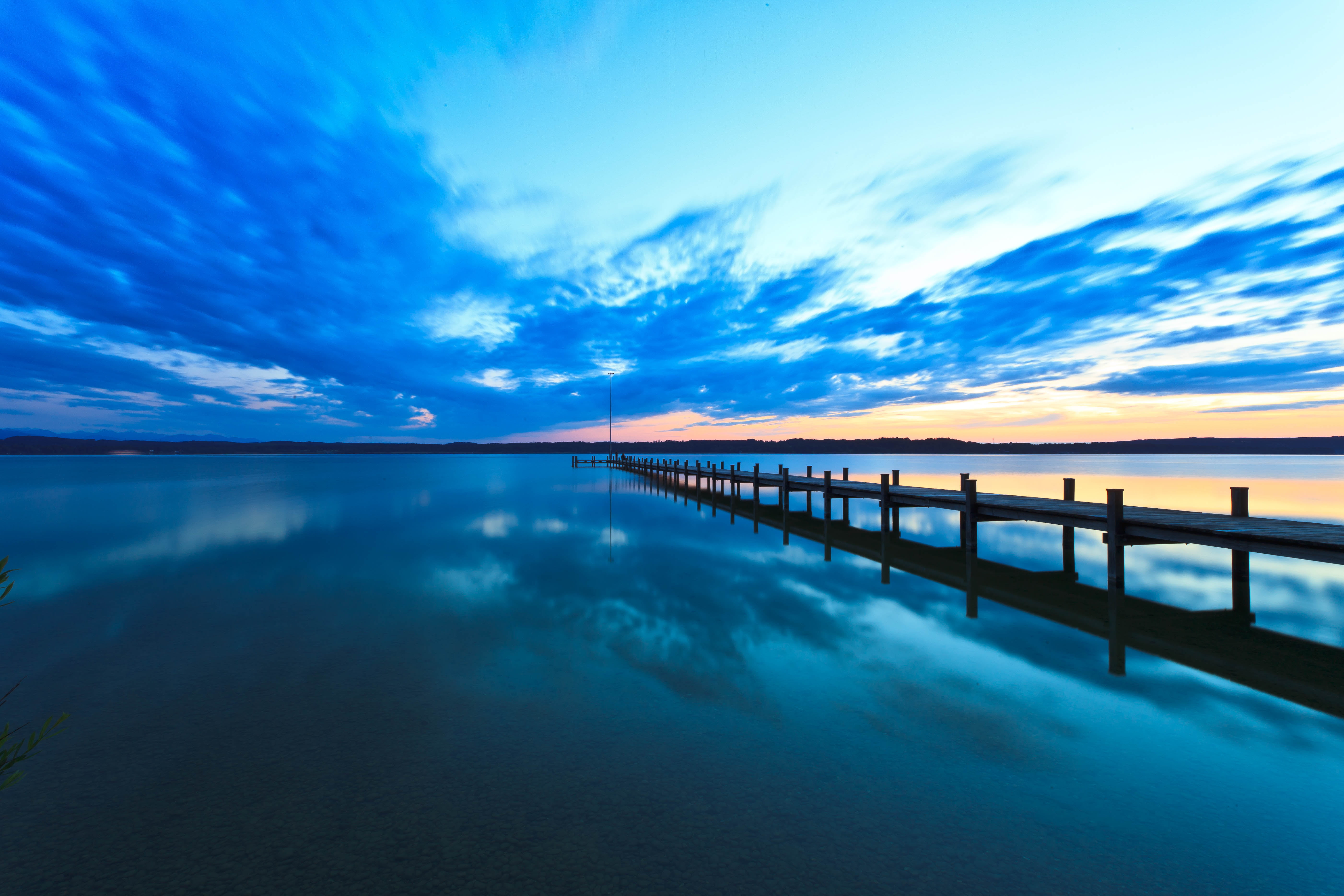 black lake dock on placid body of water under stratus clouds during golden hour 2k 4k 5k
