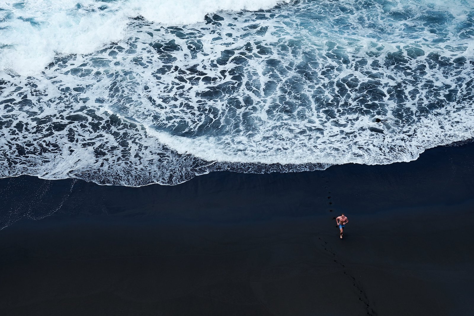 person walking on black sand near body of water beach men white 2k