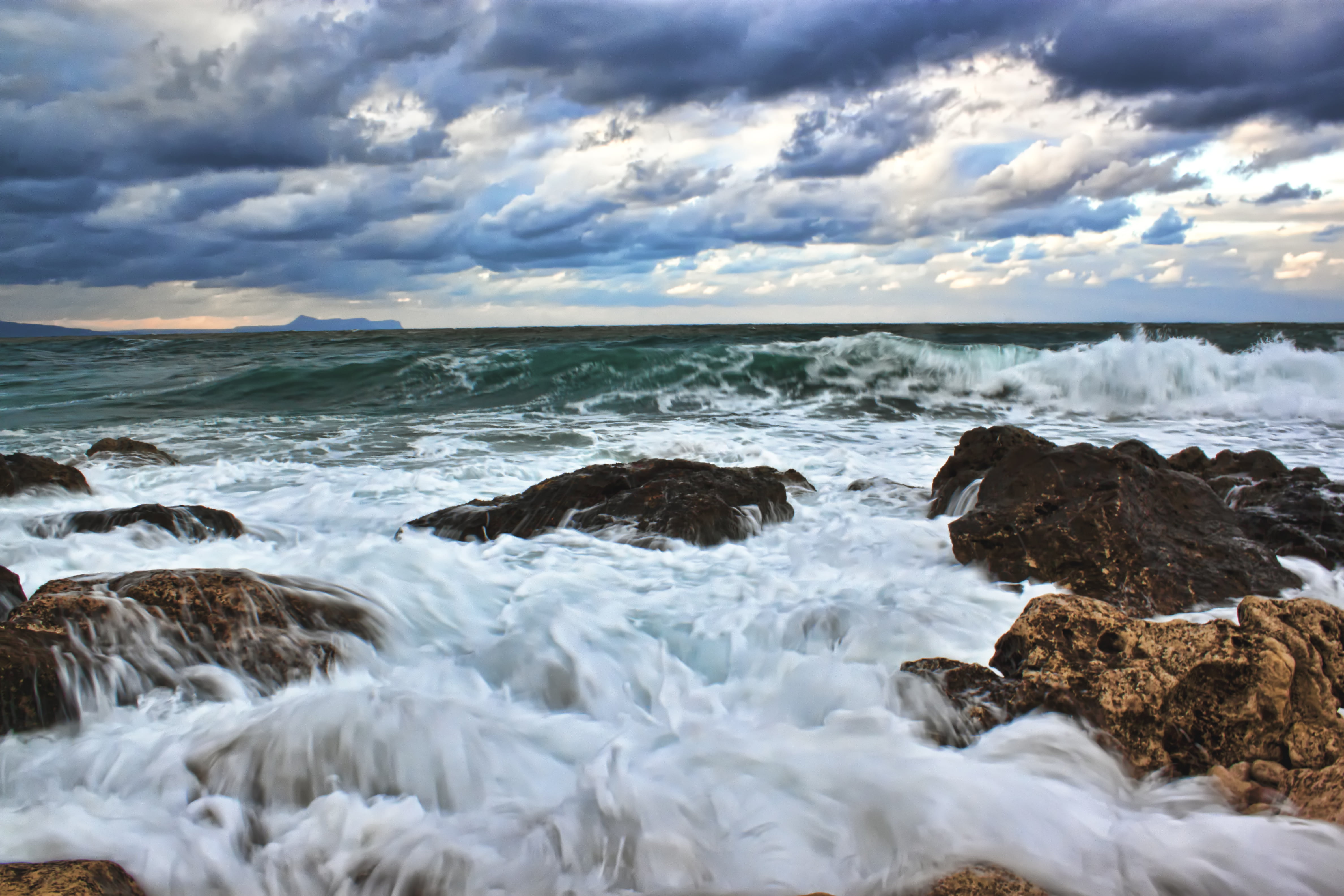 photo of wave crashing in rocky beach with gray cloudy sky background 2k 4k 5k