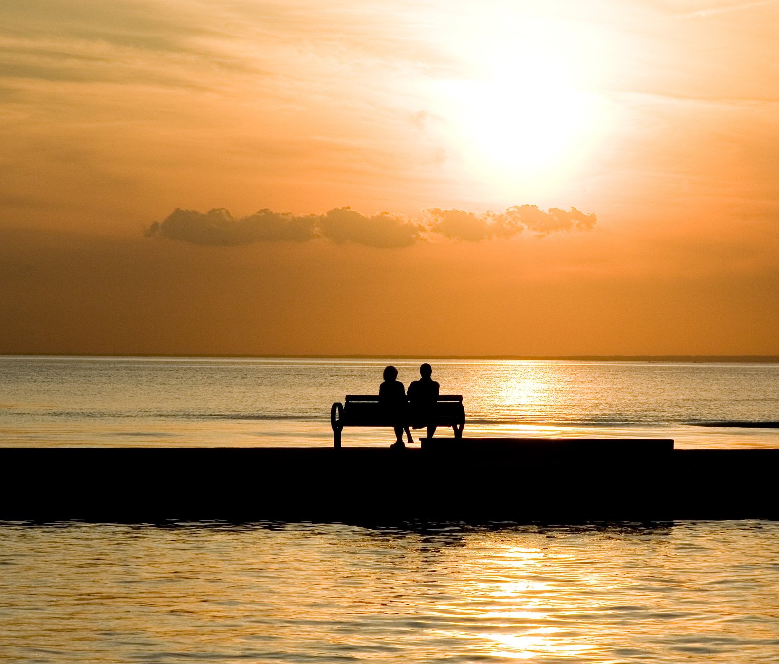 silhouette of two person sitting on bench near body water during daytime 2k