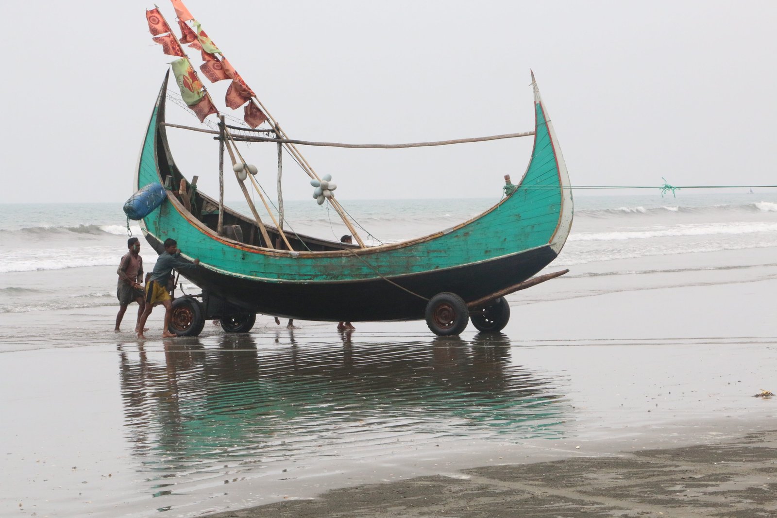 two people pushing teal and black boat cox s bazar beach 2k 4k 5k