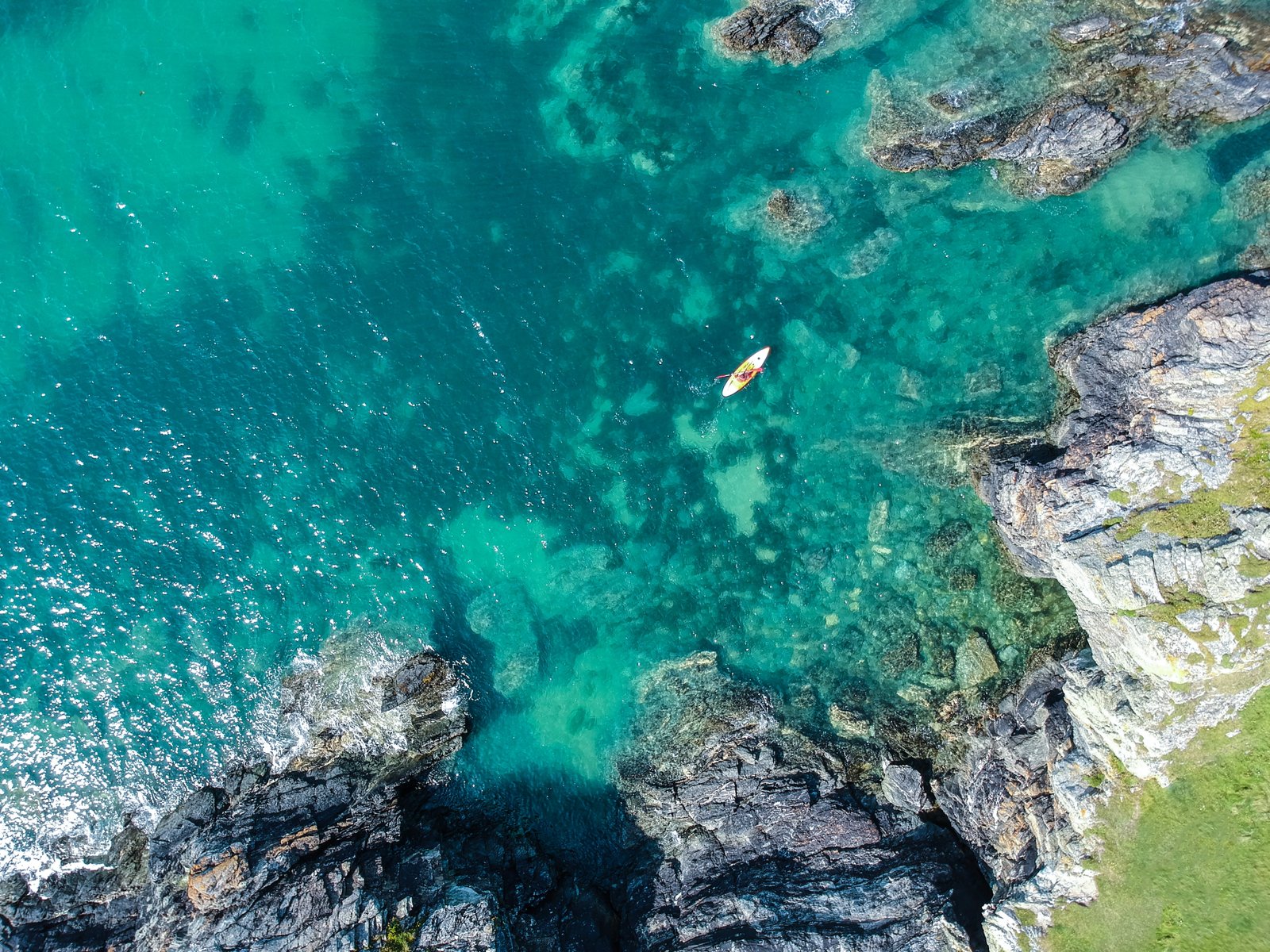 aerial view of boat on sea beside rock formation at daytime white body water surrounded gray concrete mountain rocks 2k 4k
