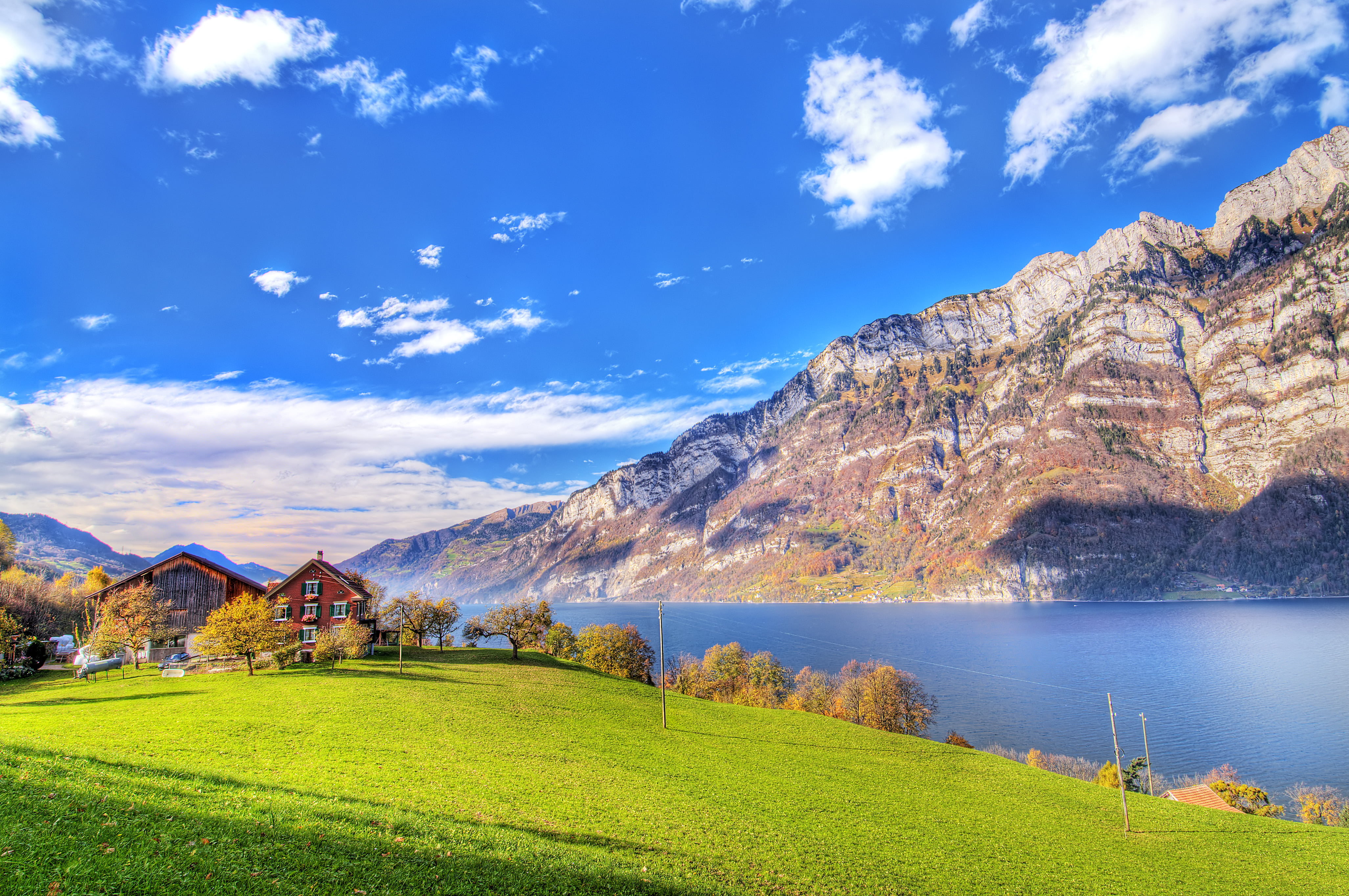brown painted house with green grass field near calm body of water mountain as background under the blue sky 2k 4k