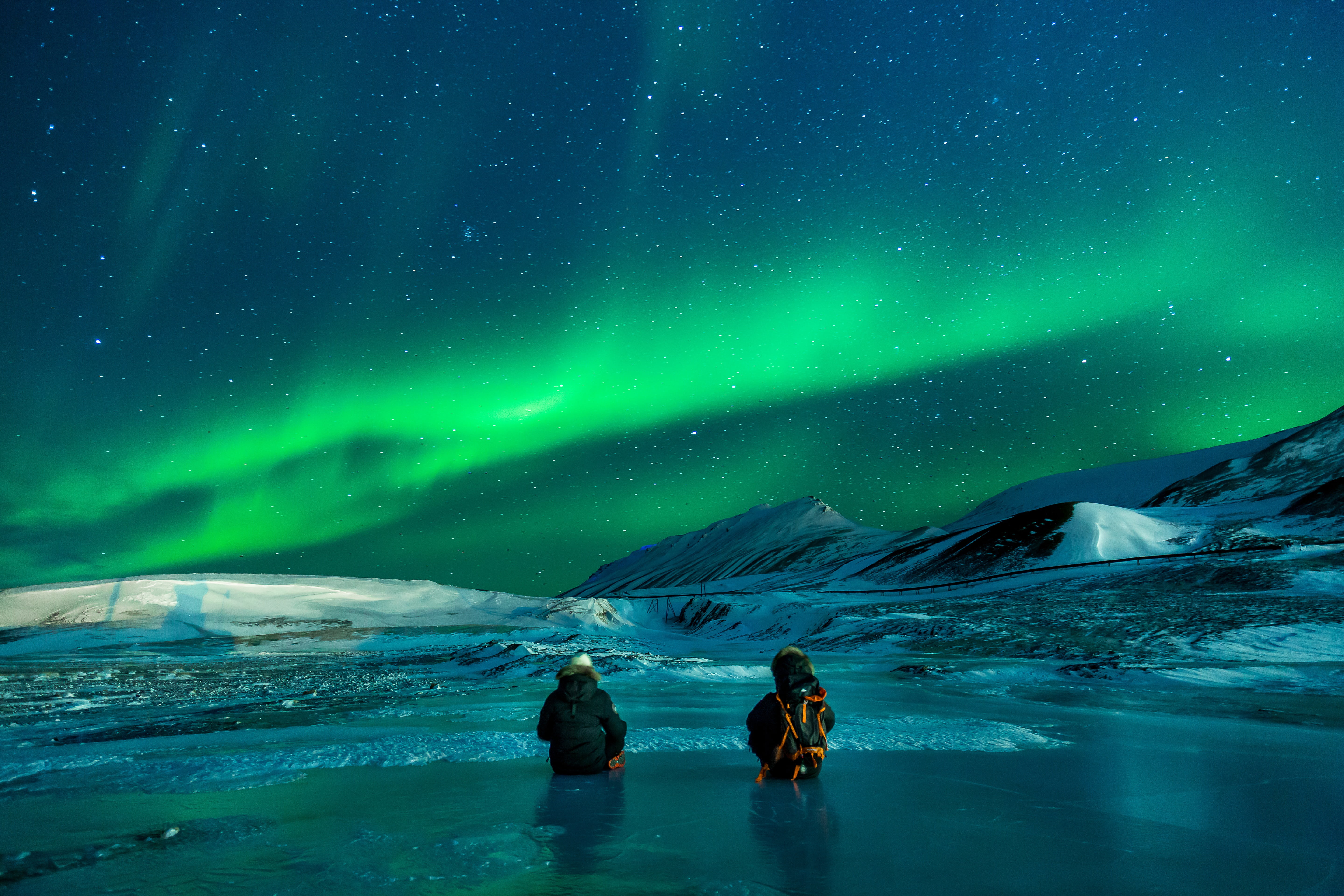 two people partially submerged on water surrounded by snow overlooking aurora borealis 2k 4k 5k