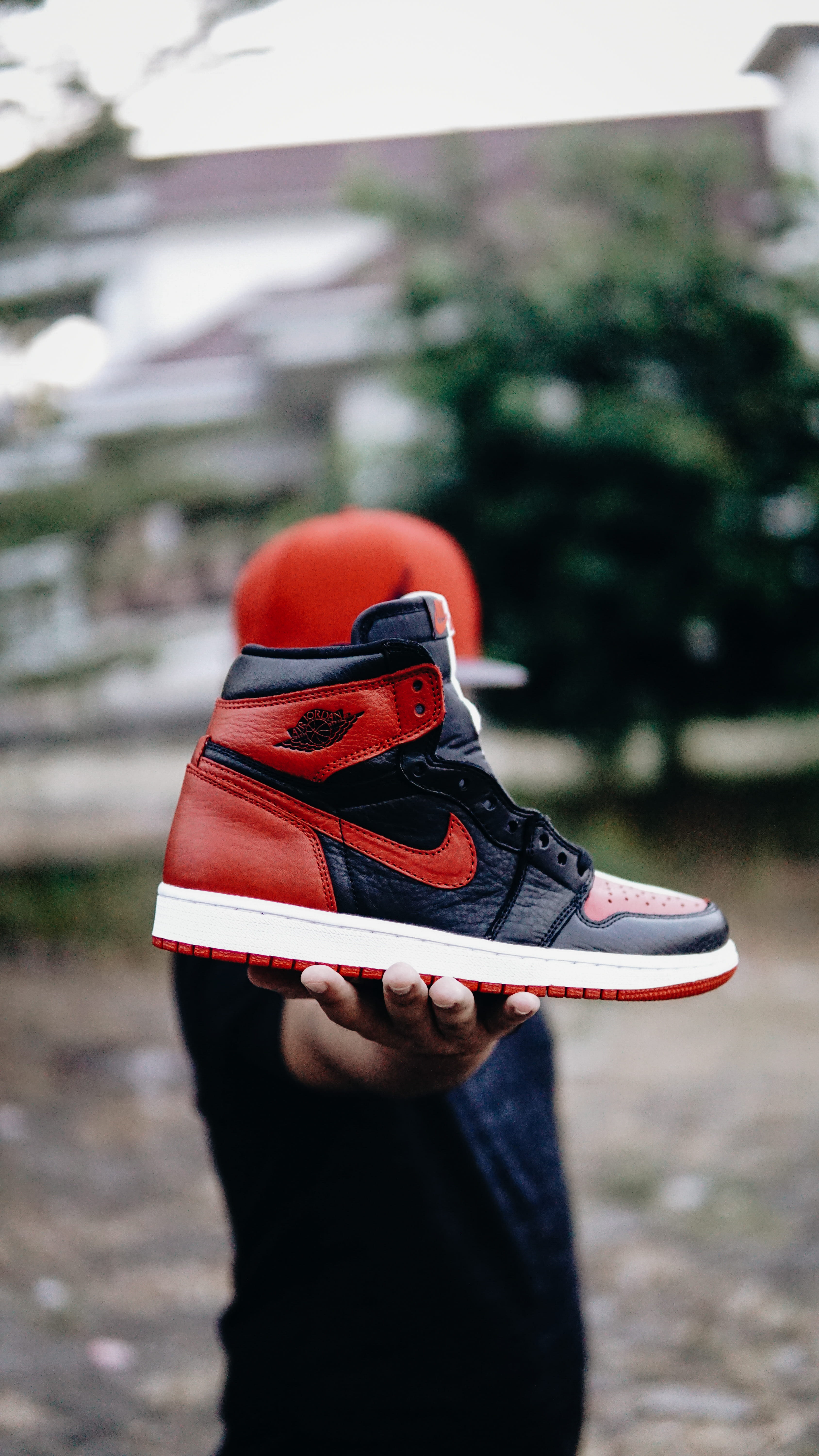 selective focus photo of person holding unpaired black and red Nike Air Jordan 1 shoe 2k