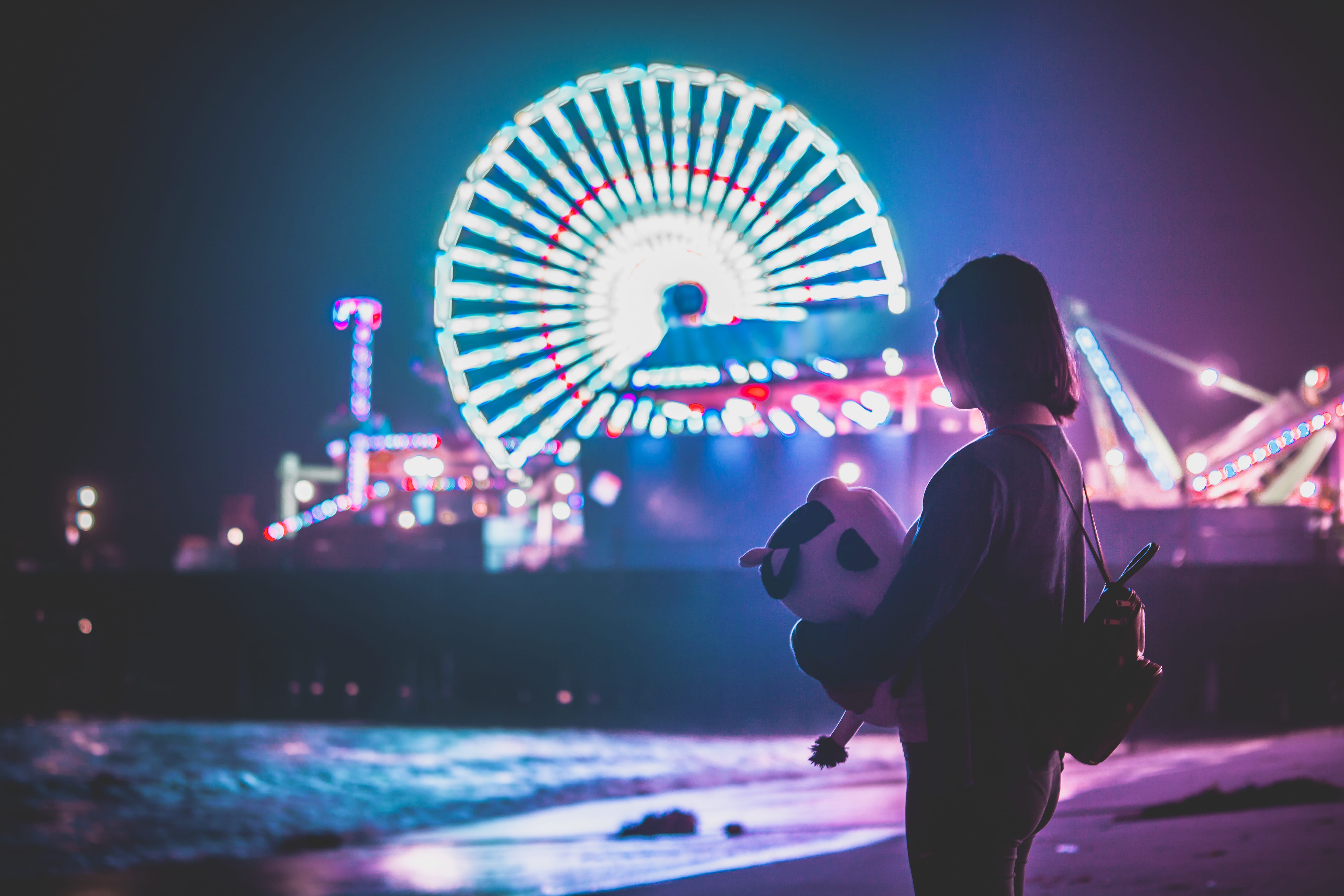 woman standing on shore near themed park during night fair beach 2k 4k 5k