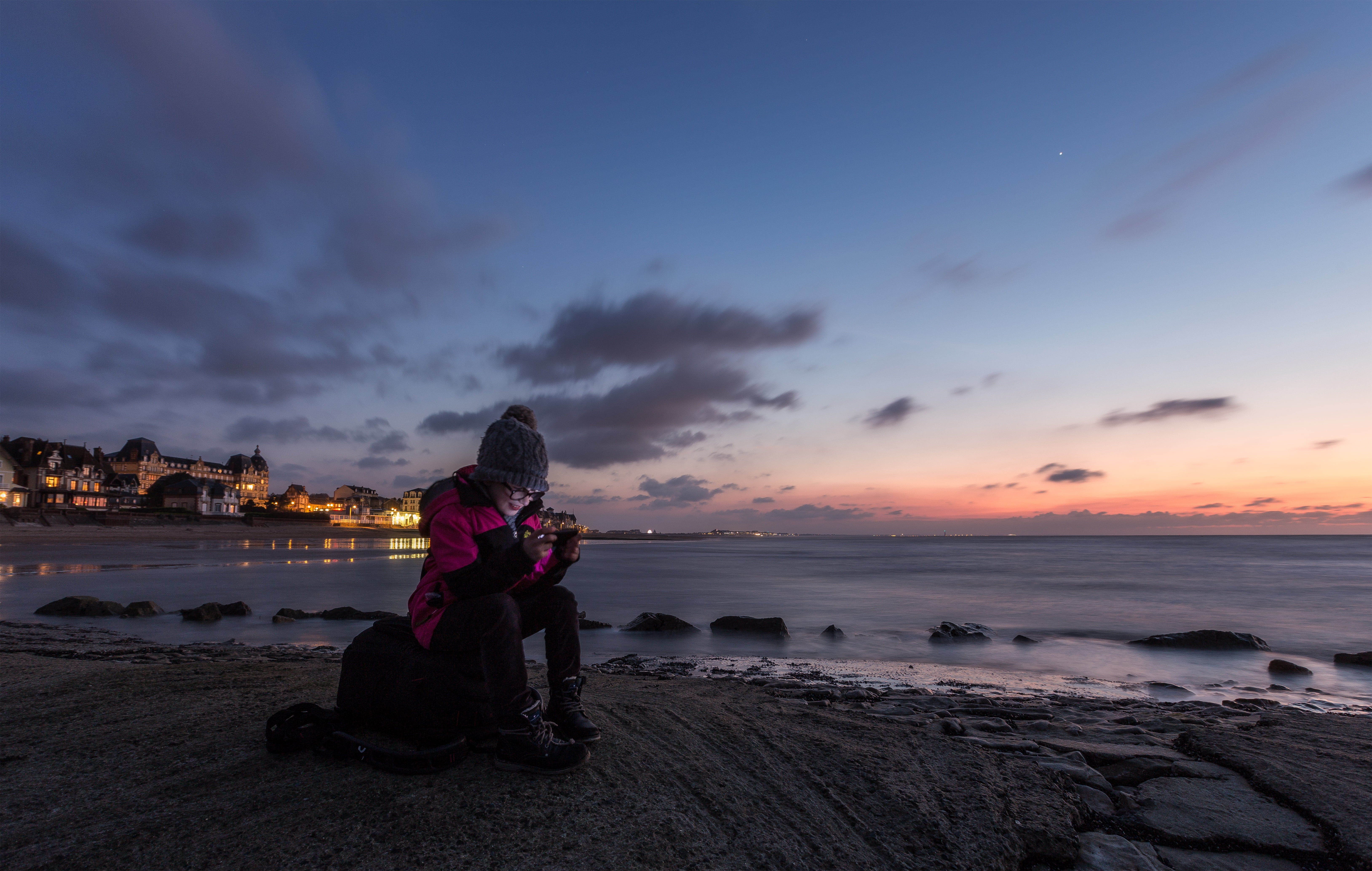 woman in pink and black winter suit sitting near body of water during yellow sunset 2k 4k 5k