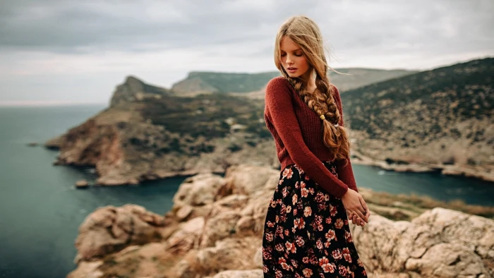 blonde haired woman in brown long sleeve top standing on of mountain beside body water 2k