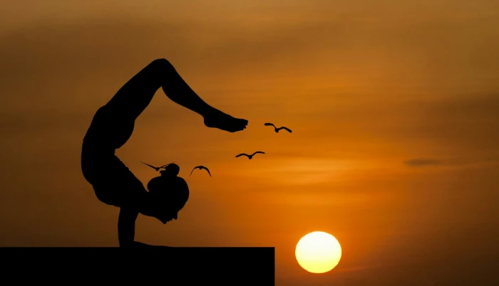 Woman doing an acrobatic yoga pose silhouetted against sunset 2k