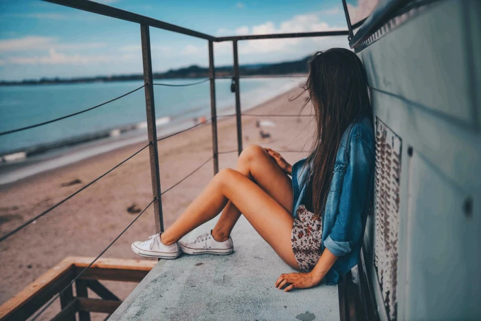 woman sitting on gray metal floor while staring at body of water during daytime 2k