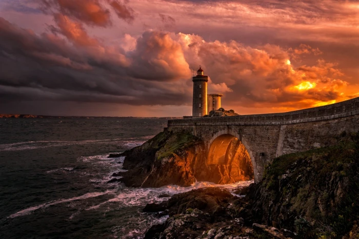 lighthouse on cliff with brown concrete bridge during golden hour 2k