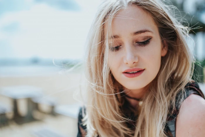 Beautiful blonde woman relaxing with a can of coke on tree stump by the beach 2k