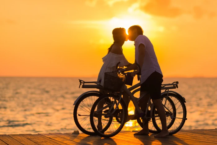 Photography of Man Wearing White T shirt Kissing a Woman While Holding Bicycle on River Dock during Sunset 2k 4k