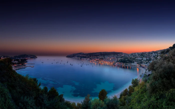 body of water surrounded with building and trees aerial photography between mountains under golden hour 2k