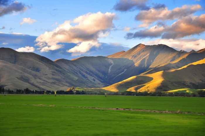 green grass field near mountain cloudy sky Landscape van 2k