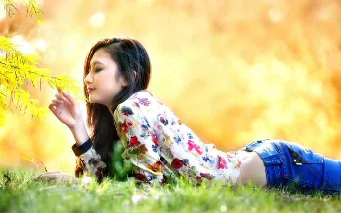 women model brunette long hair outdoors nature face trees lying on front jeans blouses asian korean smiling looking down fall grass park depth of field flowers 2k