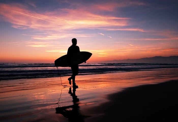 person holding surfboard while walking in the beach at night time los angeles 2k 4k