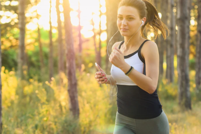 Girl jogging running exercises workout in the forest using earphones connected to her mobile iPhone smartphone 2k 4k 5k