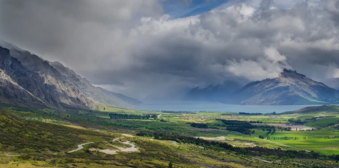 landscape photography of green and brown field surrounded by mountains gray clouds during daytime 2k 4k
