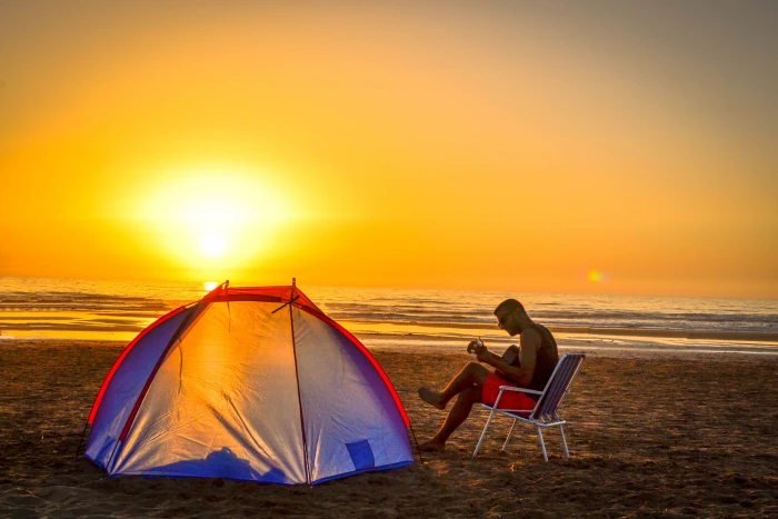 man sitting on chair playing guitar near tent beach shore during sunset 2k 4k 5k
