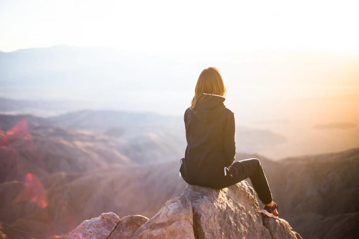 person sitting on top of gray rock overlooking mountain during daytime selective focus photography woman in track suit cliff 2k 4k 5k