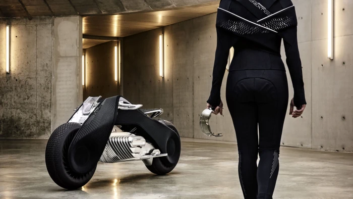 woman wearing black jumpsuit holding gray metal part standing in front of and sports bike 2k 4k